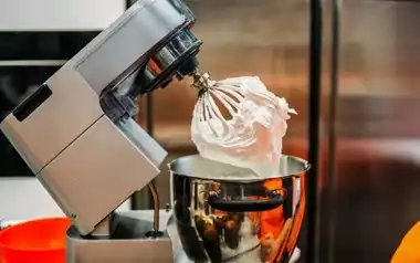 A silver stand mixer with whipped cream attached to the blender over a silver bowl.