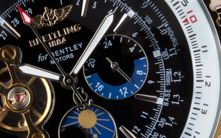 A close-up shot of a black Breitling watch face with gold and white accents and a sun within one of the dials