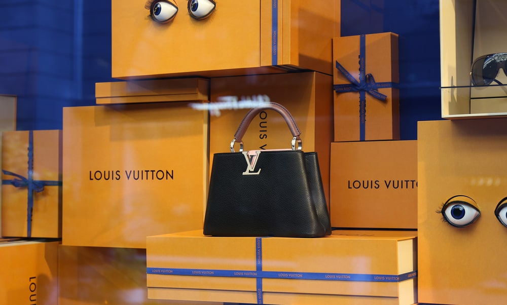 A window display of a black Louis Vuitton bag amongst an array of yellow gift boxes