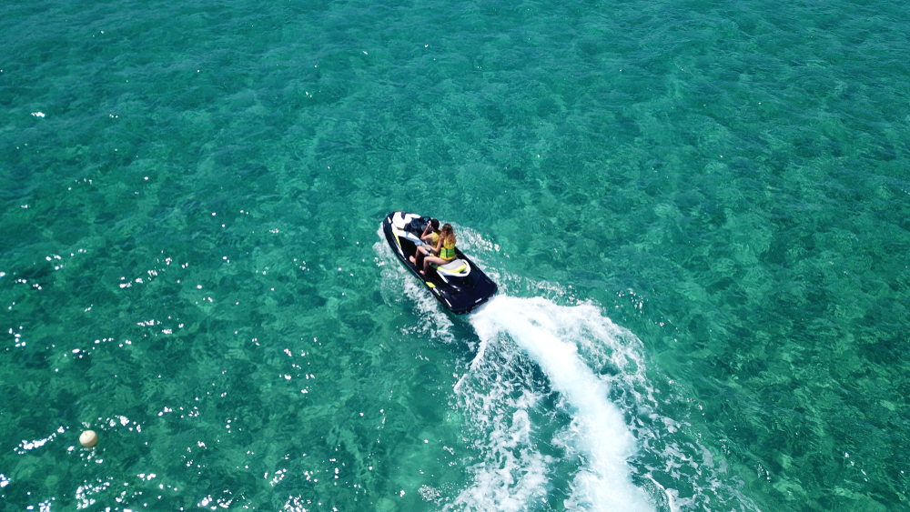 Aerial drone photo of two people on a jet ski cruising in emerald clear waters of Mykonos