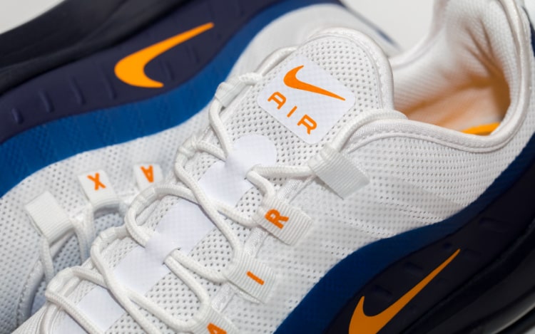 Close up of white, orange and blue trainers with neat laces. The tongue of the shoe reads AIR with a orange swoosh above it.