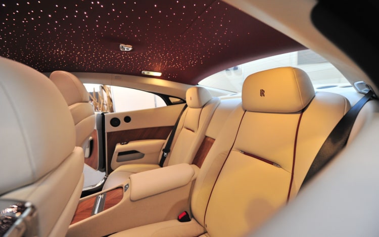 The cream leather back seats of a Rolls-Royce and a dark red ceiling dotted with fibre-optic lights.